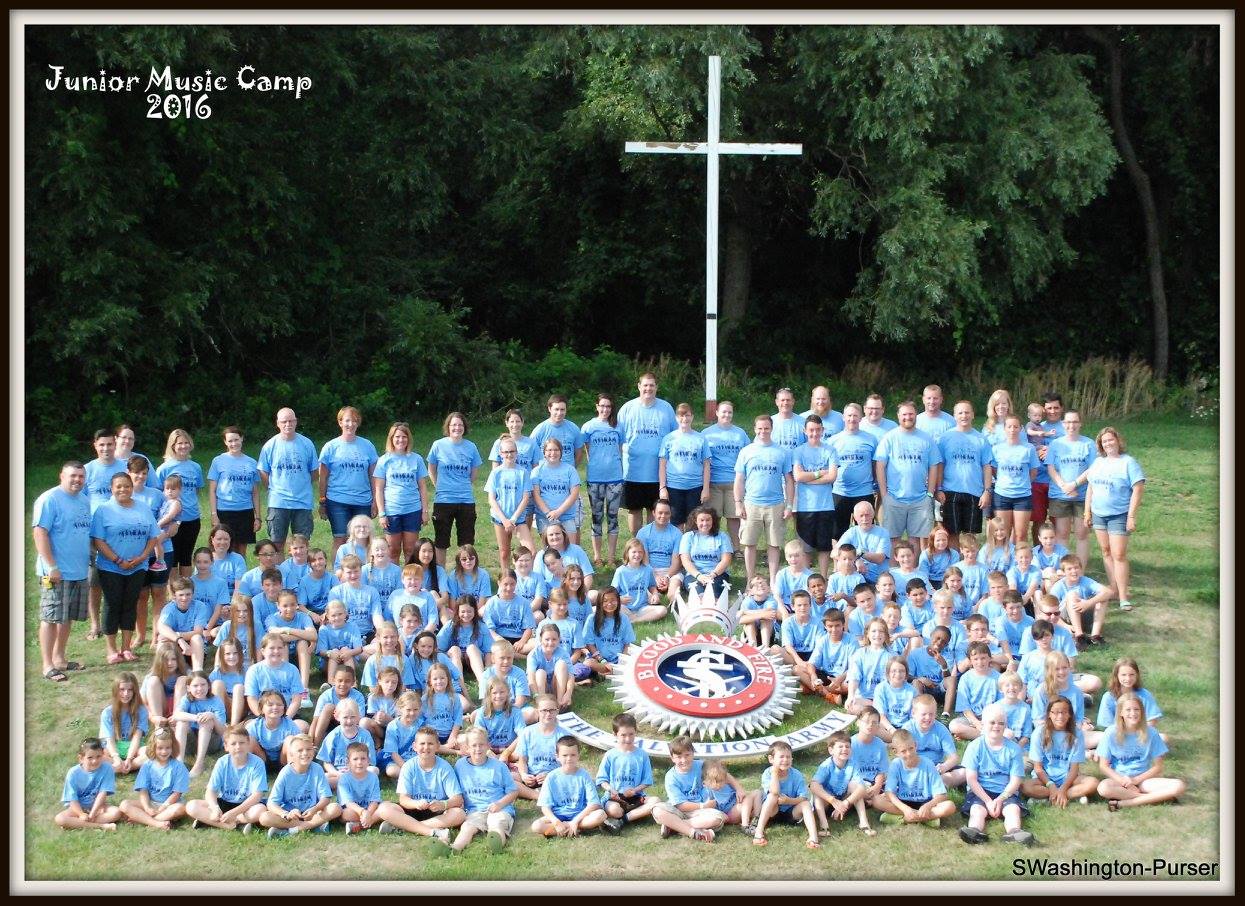 Junior Music Campers and Faculty posing around the crest and cross in the field at Jackson's Point