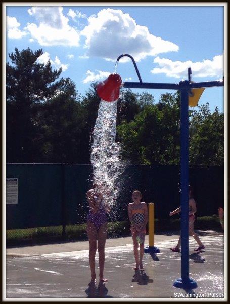 Campers standing under dumping buckets of water at the splash pad